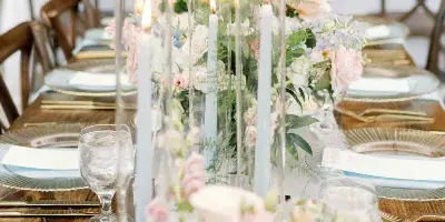 Elegant wedding table setting featuring tall glass candle holders, floral arrangements, and gold-rimmed plates.