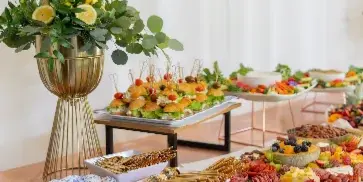 A catering buffet table featuring a tall lemon and eucalyptus centerpiece, skewered appetizers, and a charcuterie board.