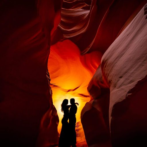 Silhouette of a couple embracing in a narrow slot canyon with warm, glowing light.
