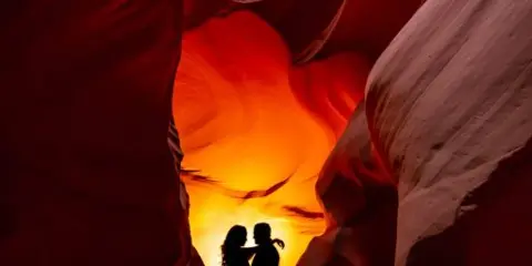 Silhouette of a couple embracing in a narrow slot canyon with warm, glowing light.