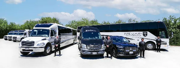 A lineup of Pure Luxury Transportation vehicles including a white coach bus, a black Mercedes van, and a black SUV, with staff members standing in front.