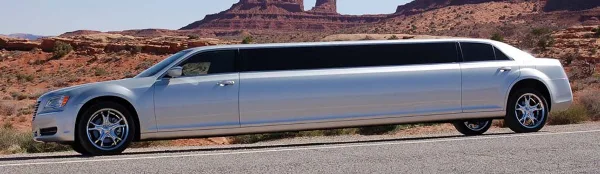 A silver stretch limousine parked on a road with a rocky landscape in the background.
