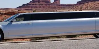 A silver stretch limousine parked on a road with a rocky landscape in the background.