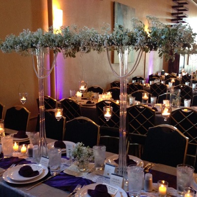 A wedding reception room with tall floral centerpieces, candles, and decorated tables.