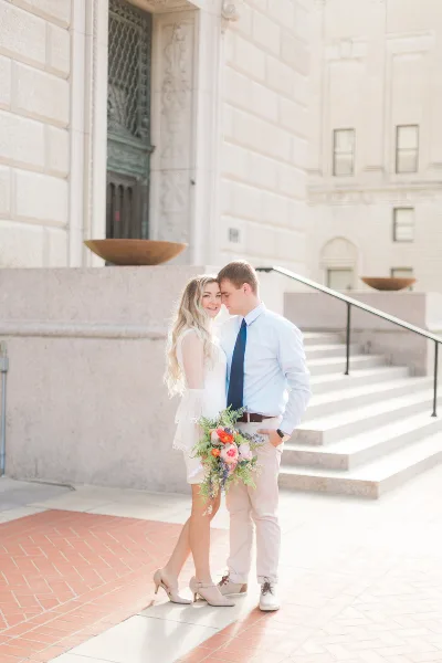 A professional photograph of a bride and groom standing together outdoors in front of a stone building.