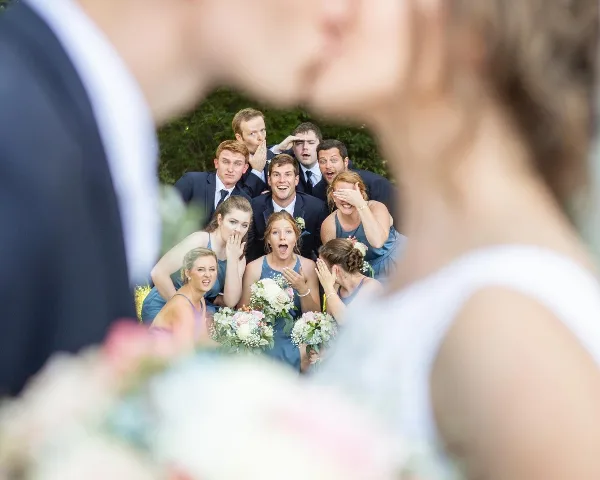 A wedding party consisting of bridesmaids in blue dresses and groomsmen in suits posing outdoors with bouquets.