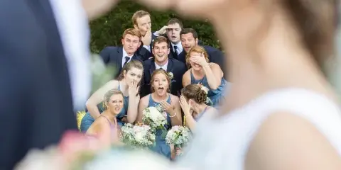A wedding party consisting of bridesmaids in blue dresses and groomsmen in suits posing outdoors with bouquets.