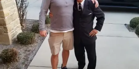 A professional chauffeur in a suit posing with a client in front of a black SUV.