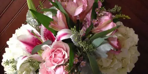 A floral arrangement with pink lilies, pink roses, and white hydrangeas in a square glass vase.