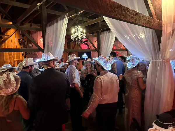 Guests wearing cowboy hats dancing at a wedding reception in a barn venue.