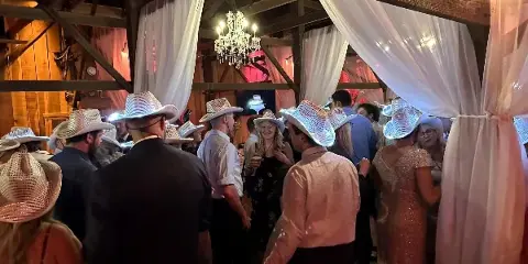 Guests wearing cowboy hats dancing at a wedding reception in a barn venue.
