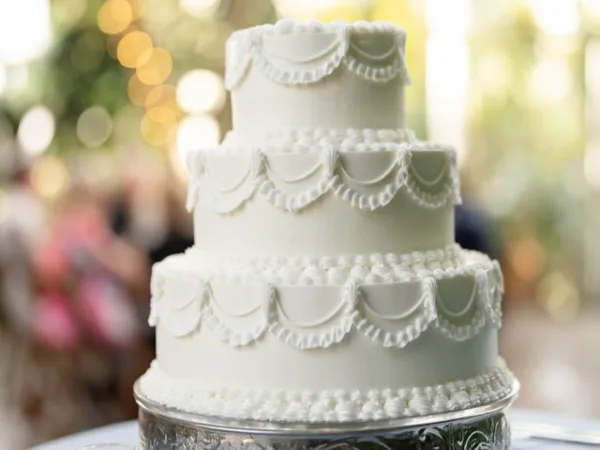 A three-tiered white wedding cake with decorative piping details on a silver stand.
