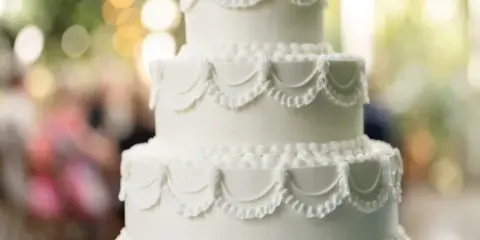 A three-tiered white wedding cake with decorative piping details on a silver stand.