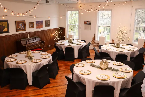An indoor event space set up for a wedding reception with round tables, white tablecloths, and string lights.