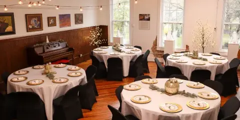 An indoor event space set up for a wedding reception with round tables, white tablecloths, and string lights.