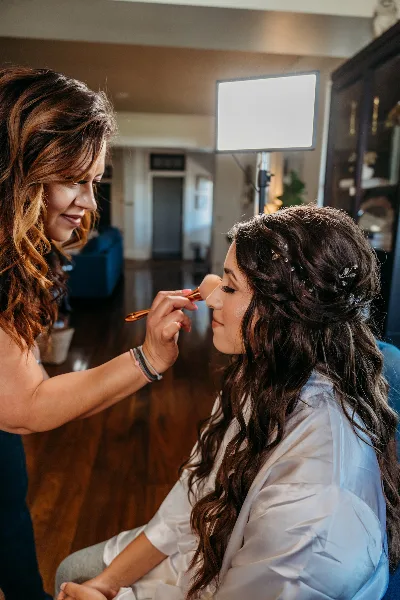 A makeup artist applying makeup to a bride in a studio setting.