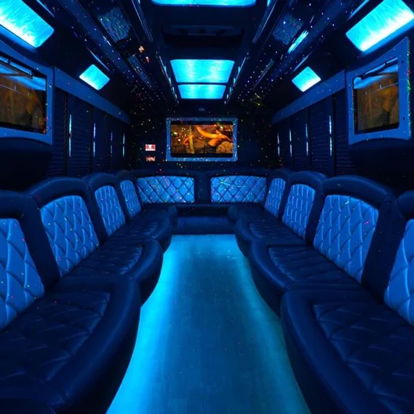 Interior of a party bus featuring blue ambient lighting, quilted leather seating, and a central entertainment screen.