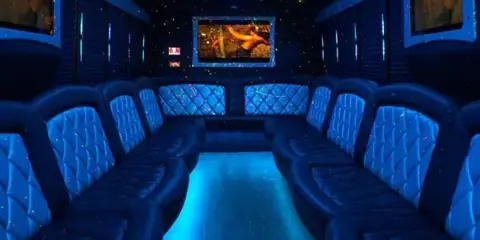 Interior of a party bus featuring blue ambient lighting, quilted leather seating, and a central entertainment screen.