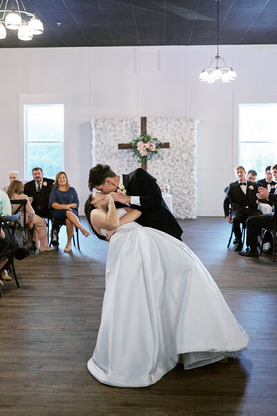 A bride and groom dancing during a wedding reception in a large indoor event space with guests watching.