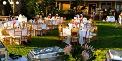 Outdoor catering event featuring buffet chafing dishes and a decorated venue with tables and chairs.