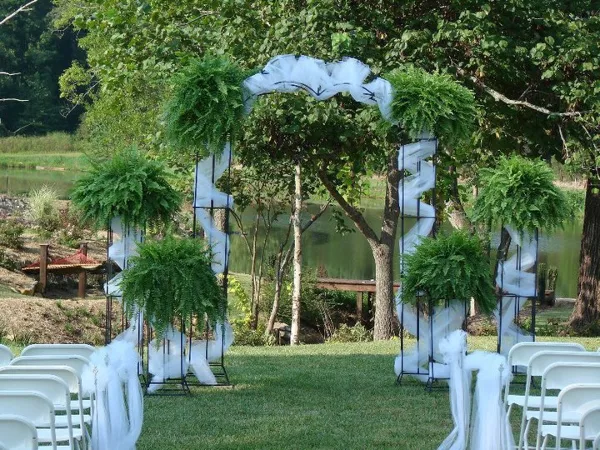 Outdoor wedding ceremony setup with a floral arch and white chairs near a body of water.