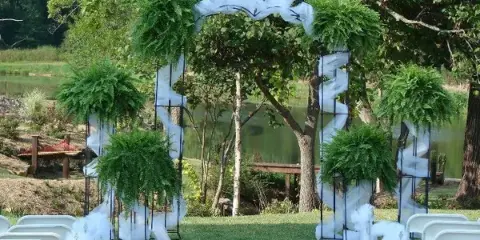 Outdoor wedding ceremony setup with a floral arch and white chairs near a body of water.