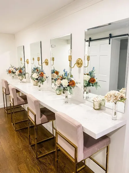 A bridal suite vanity area with a white marble counter, gold-framed mirrors, and floral arrangements.