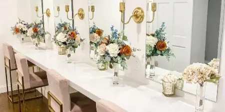 A bridal suite vanity area with a white marble counter, gold-framed mirrors, and floral arrangements.