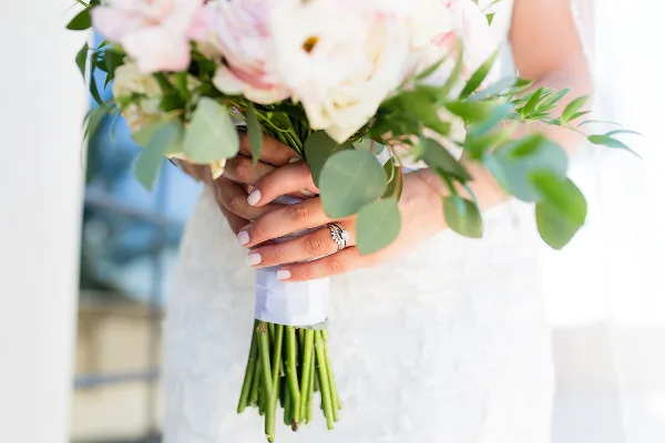 Close-up of a bride's hands holding a bouquet of white and pink flowers with greenery.