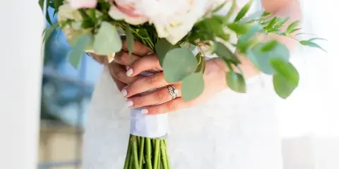 Close-up of a bride's hands holding a bouquet of white and pink flowers with greenery.