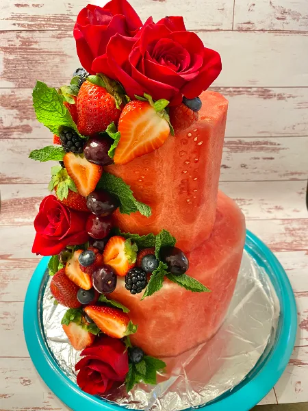 A two-tier pink cake decorated with fresh strawberries, red roses, and mint leaves.