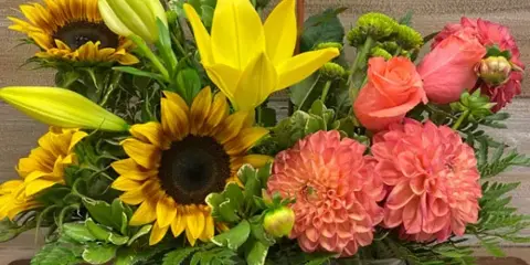 A floral arrangement with sunflowers, yellow lilies, and pink roses in a wire basket with a cow silhouette tag.