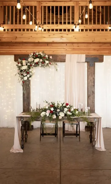 Rustic wedding sweetheart table with floral arrangements and a wood backdrop