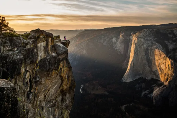 A couple standing on a rocky ledge overlooking Yosemite Valley at sunset.