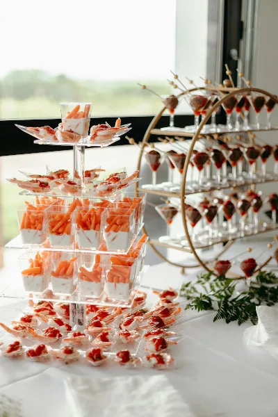 A catering table featuring a tiered stand of shrimp appetizers and a gold stand holding small dessert cups.