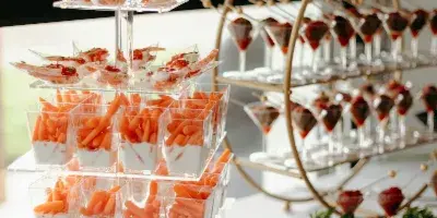 A catering table featuring a tiered stand of shrimp appetizers and a gold stand holding small dessert cups.
