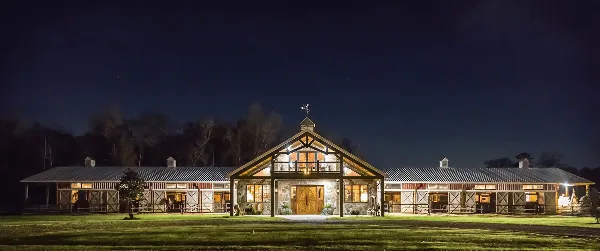 Exterior view of a large, illuminated barn venue at night with a grassy foreground.