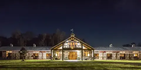 Exterior view of a large, illuminated barn venue at night with a grassy foreground.