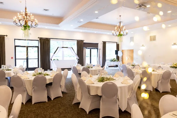 Interior view of a wedding venue with round tables, white linens, and chandeliers.