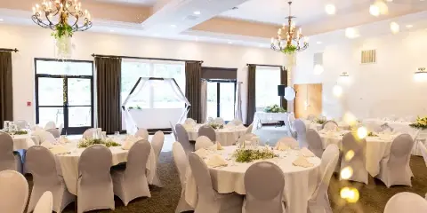 Interior view of a wedding venue with round tables, white linens, and chandeliers.