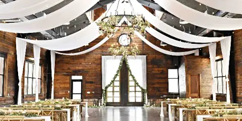 Interior of a rustic wooden barn wedding venue with white ceiling drapery, floral chandelier, and reception tables.
