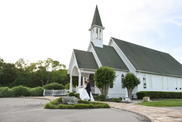 A bride and groom standing together in front of a white church with a steeple.