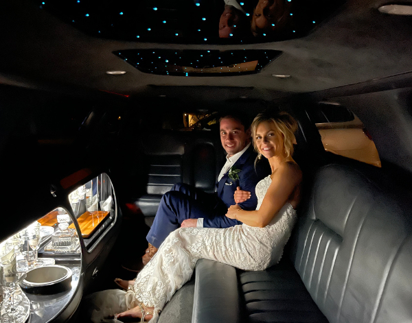 Bride and groom seated inside a luxury limousine with starlight ceiling and bar setup