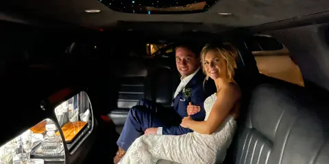 Bride and groom seated inside a luxury limousine with starlight ceiling and bar setup