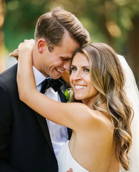 A smiling bride with styled hair and makeup embracing a groom in a tuxedo.