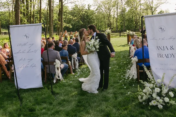 A bride and groom kissing during an outdoor wedding ceremony with guests seated on either side.