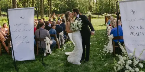 A bride and groom kissing during an outdoor wedding ceremony with guests seated on either side.