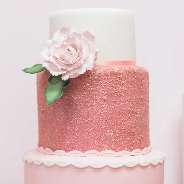 A three-tiered wedding cake featuring a pink glitter middle tier, white top tier, and a large fondant flower decoration.