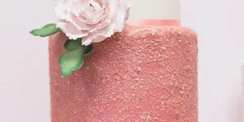 A three-tiered wedding cake featuring a pink glitter middle tier, white top tier, and a large fondant flower decoration.