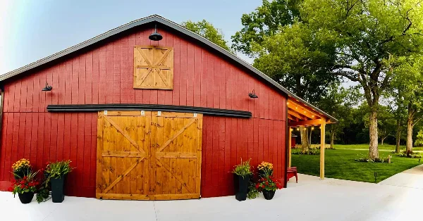 Exterior view of a red wooden barn venue with a covered patio and potted flowers.
